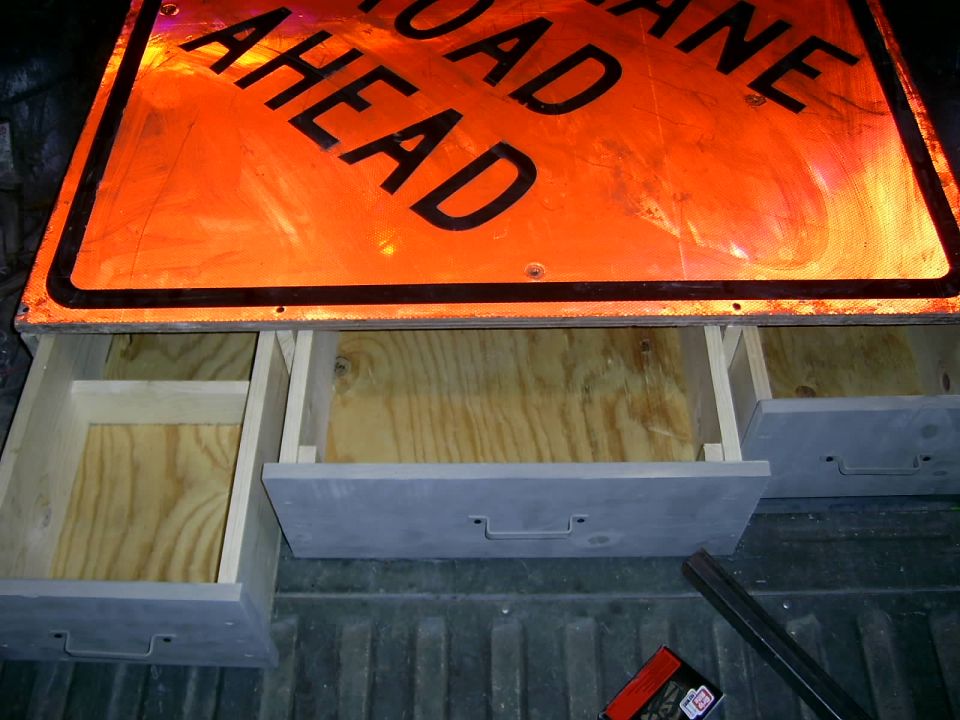 Storage drawers installed in the bed of a pickup truck, beneath an orange road sign
