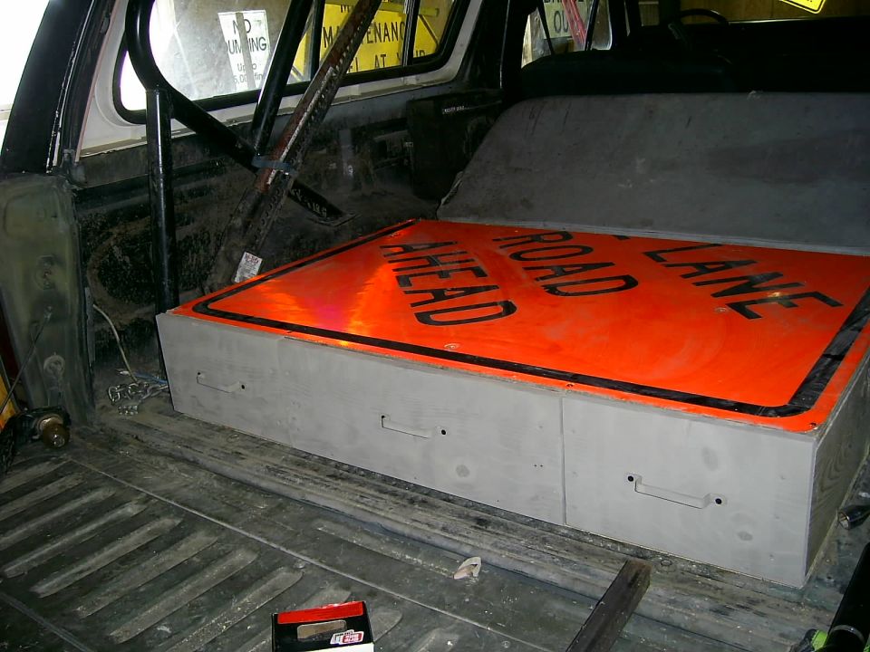 Interior view of a vehicle cargo area with a storage box topped by a 'Road Ahead Lane' traffic sign