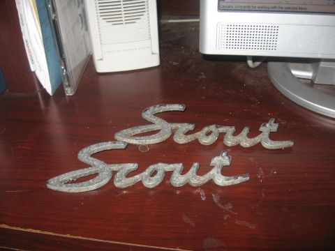 1996 Ford Bronco - Two metal Scout emblems are shown on a dark wood surface next to computer equipment.