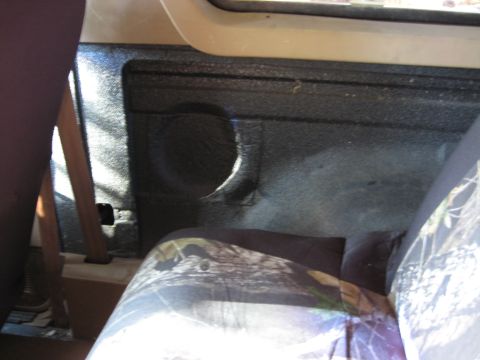 1990 Ford Bronco - The interior rear panel of a vehicle shows a speaker cutout and a camouflage seat cover is visible in the foreground.