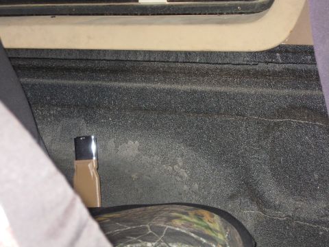 1990 Ford Bronco - Close-up of a truck bed's textured coating and a camouflage seat cover, with a small black and tan object visible.