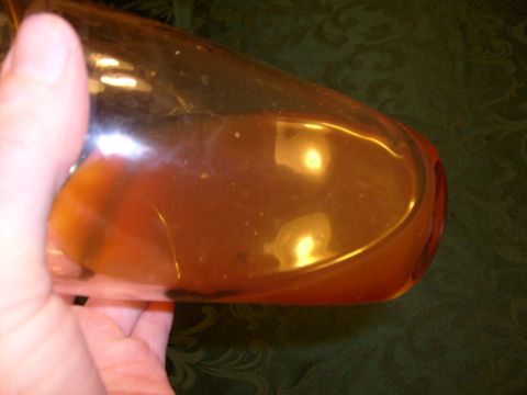 1995 Ford C-350 (Centurion Conversions) - A close-up view of an amber glass part being held by a hand against a dark green patterned background.
