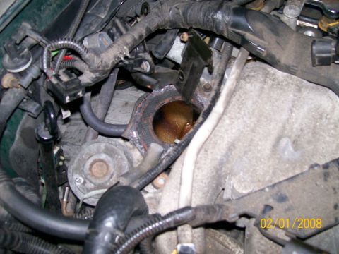 1995 Mercury Grand Marquis - Engine bay detail shot looking down at an open exhaust manifold flange with a rusty port and gasket exposed after removal of a component, s…