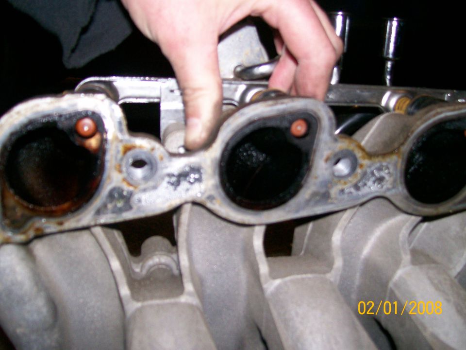 Intake manifold gasket with four ports, showing carbon buildup and orange seals