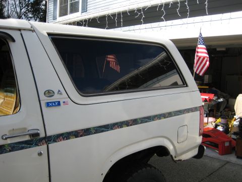 1980 Ford Bronco - Side view of a white SUV with a camouflage stripe and an American flag displayed inside.
