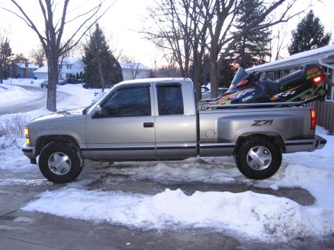 1998 GMC Sierra 1500 - A silver 1998 GMC Sierra 1500 pickup truck is parked in a snowy driveway with a snowmobile loaded in the bed.