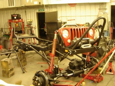 1991 Ford Bronco - A red Jeep Wrangler front end and chassis are disassembled in a workshop, with the year 2006 visible on a floor jack.