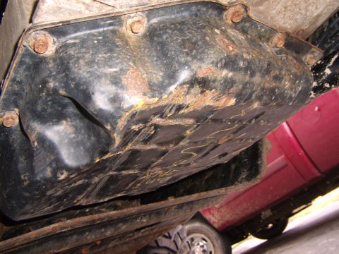 2003 Jeep Wrangler - Underside view of a heavily rusted transmission pan, showing bolts and some faint yellow markings.
