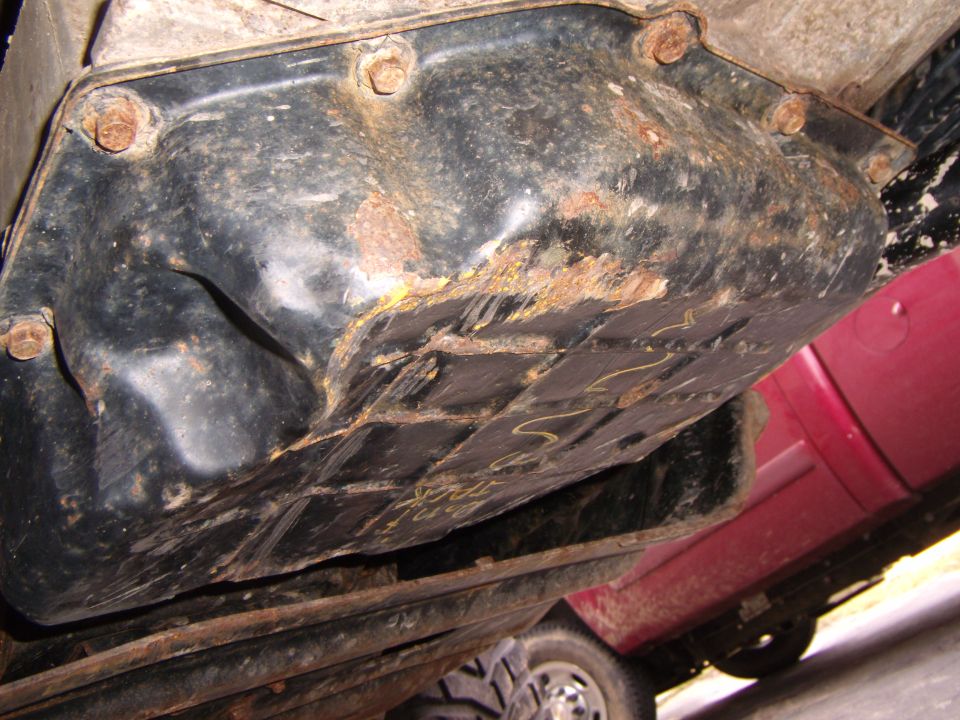 Rusted transmission pan with bolts and some yellow markings