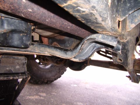 2003 Jeep Wrangler - The underside of a vehicle shows the transmission pan and exhaust system, with a jack supporting the frame.
