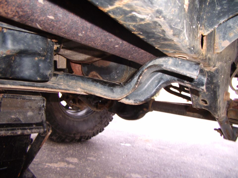 Underbody of a vehicle with a black transmission pan, exhaust pipe, and suspension components. A jack is visible on the left