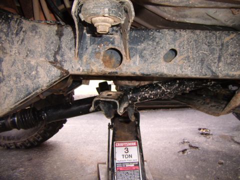 2003 Jeep Wrangler - A hydraulic floor jack supports the underbody of a vehicle, showing suspension and frame components.