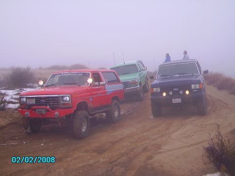 1990 Ford Bronco - Three SUVs are seen on a dirt road in foggy conditions.