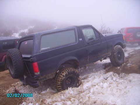 1990 Ford Bronco - A 1990 Ford Bronco navigates a snowy, off-road trail with another vehicle visible in the background.