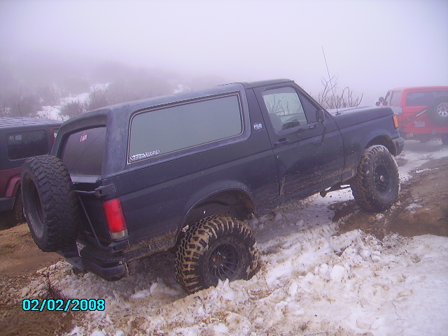 Dark Ford Bronco driving through snow with a red SUV behind it