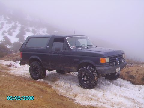 1990 Ford Bronco - A dark blue 1990 Ford Bronco navigates a snowy, off-road path, its capabilities.