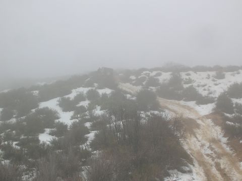 1985 Ford Bronco - A vehicle is barely visible on a remote, foggy, and snow-dusted hillside with a dirt track.