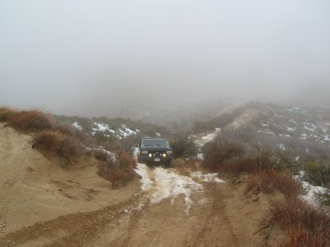 1985 Ford Bronco - 1985 Ford Bronco navigates a challenging off-road path in foggy, wintry conditions.