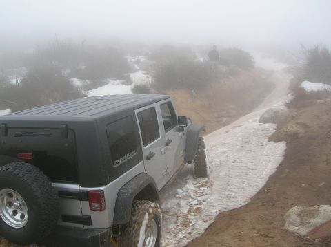 1985 Ford Bronco - A Jeep Wrangler navigates a challenging off-road trail covered in snow and mud.