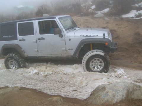1985 Ford Bronco - A silver Jeep Wrangler Rubicon navigates through a snowy and muddy off-road trail.