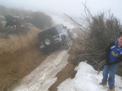 1985 Ford Bronco - A Jeep Wrangler is stuck on a treacherous dirt road covered in mud and snow, with two people nearby.