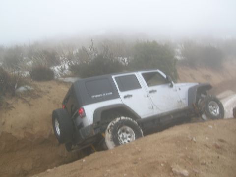 1985 Ford Bronco - Jeep Wrangler navigates a sandy, rutted trail in foggy conditions.