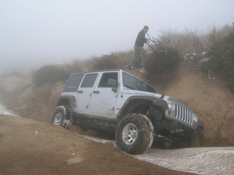 1985 Ford Bronco - A Jeep navigates a challenging off-road path in foggy conditions.