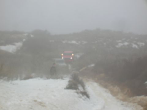 1985 Ford Bronco - A red SUV drives through fog and snow on a dirt road, its headlights illuminated.