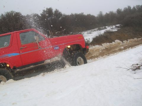 1985 Ford Bronco - A red Ford Bronco navigates a snowy, muddy trail, kicking up snow and dirt.