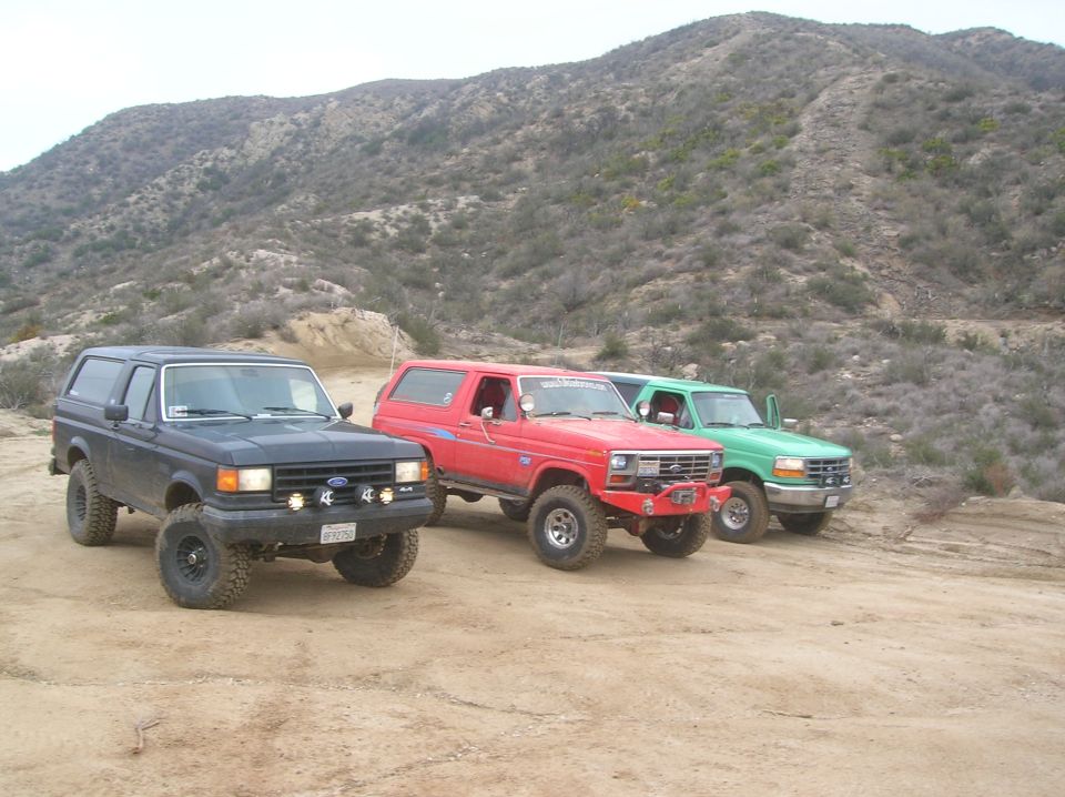 Three Ford Bronco SUVs parked on a dirt road with a hilly, scrub-covered landscape behind them