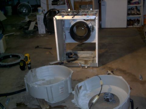 2005 Ford Mustang - A washing machine is taken apart in a cluttered garage space, with its drum and outer casing separated.