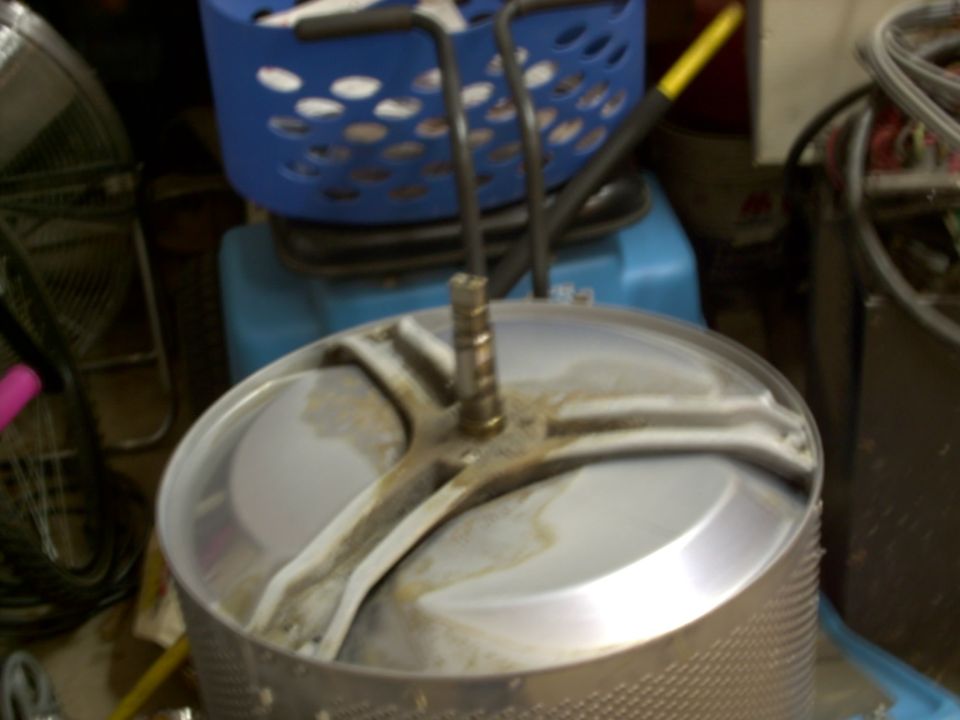 Washing machine drum with a metal agitator shaft and a blue laundry basket in the background