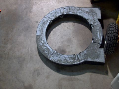 2005 Ford Mustang - A circular gray part is shown on a concrete floor, with a tire visible to its right.