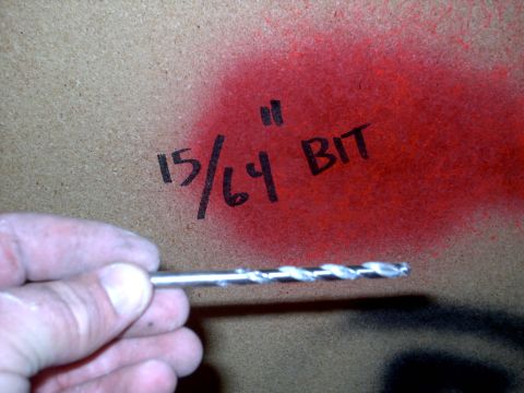 2005 Ford Mustang - A hand holds a drill bit in front of a particle board surface marked with spray paint.