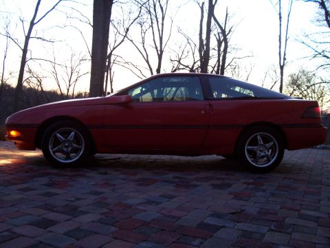 1989 Ford Probe - A red 1989 Ford Probe is parked on a brick driveway with trees in the background.