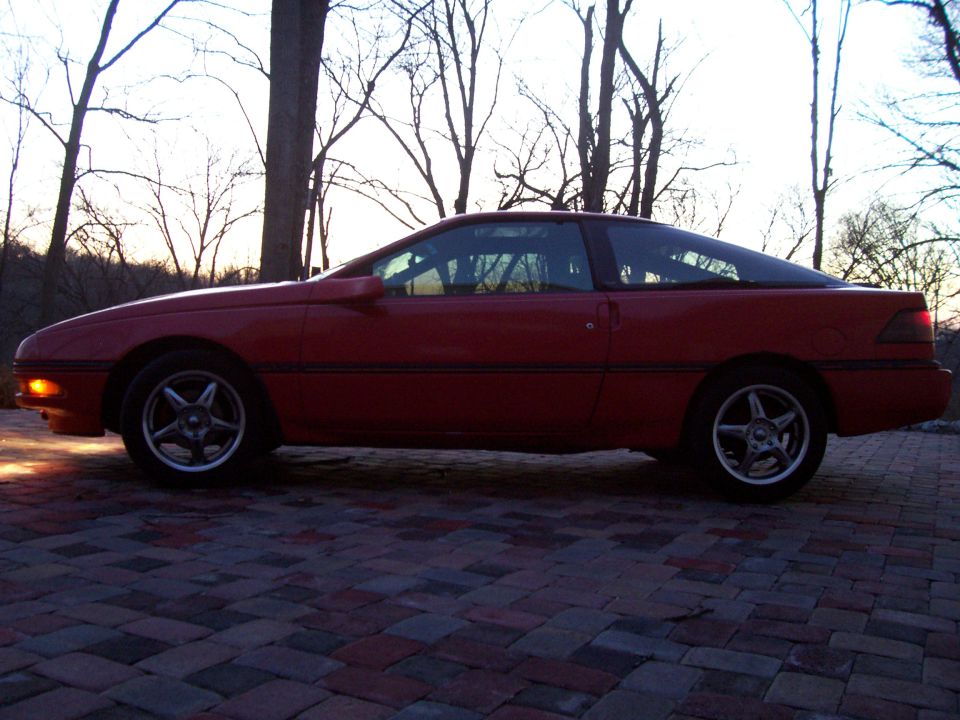 Red 1989 Ford Probe parked on brick pavers, side view