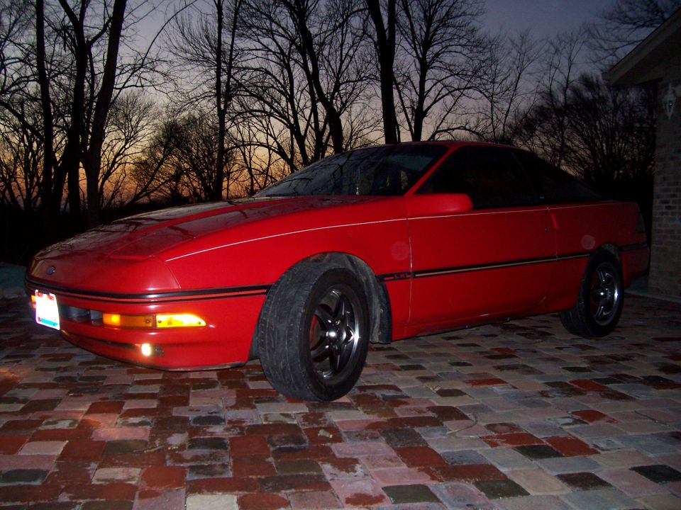 Red 1989 Ford Probe coupe parked on brick driveway at dusk