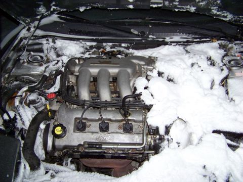 1996 Ford Probe - The engine compartment is heavily covered in snow, obscuring most of the engine details.