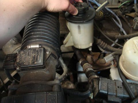1996 Ford Bronco - A hand tightens the cap on the power steering fluid reservoir of a 1996 Ford Bronco in its engine bay.