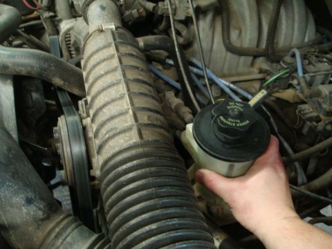 1996 Ford Bronco - A hand holds the power steering fluid reservoir in a vehicle's engine bay. The cap has instructions not to overfill the fluid.