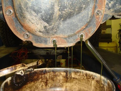 1996 Ford Bronco - Old differential fluid is being drained from a rusty rear axle cover into a catch pan.