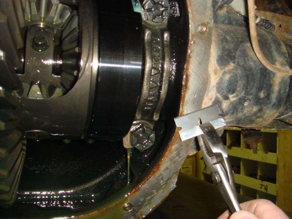 Close-up of a vehicle's differential housing being scraped with a razor blade held by pliers