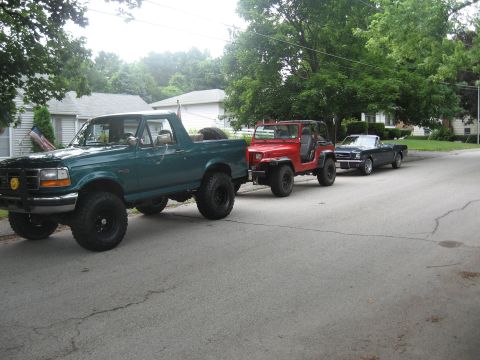 1996 Ford Bronco - Three vehicles parked on a residential street: a green 1996 Ford Bronco, a red Jeep, and a dark blue convertible.