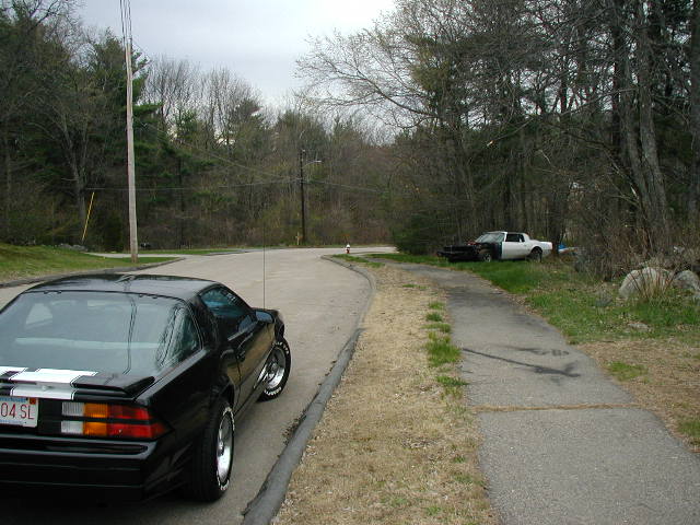 Black 1988 Chevrolet Camaro parked on a road, with a white pickup truck in the background