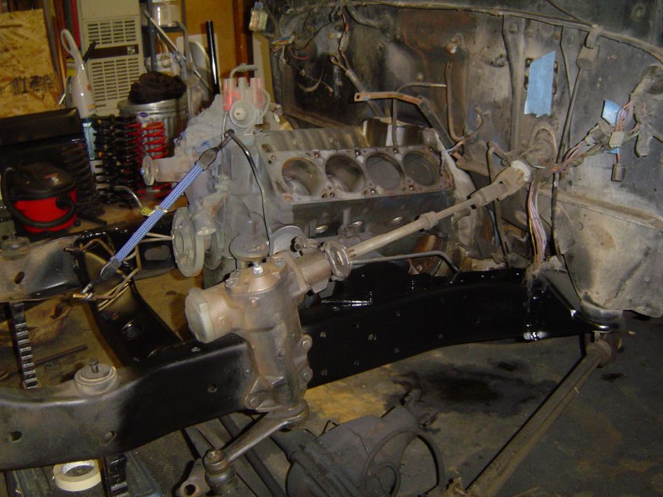 Engine block, steering box, and frame rails of a vehicle undergoing restoration. Wires and hoses are disconnected