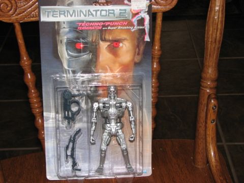 1991 Ford Bronco - A Terminator 2 action figure is displayed in its original packaging, complete with accessories, resting on a wooden chair.