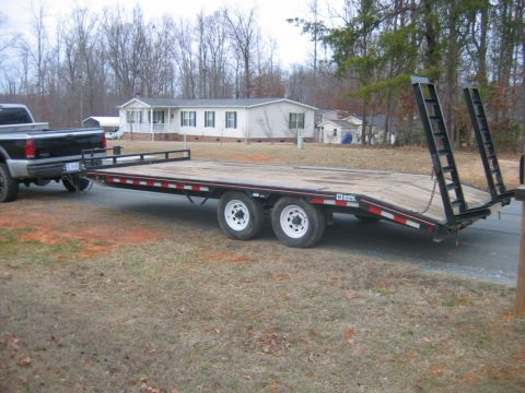 1992 Ford Mustang - A pickup truck tows a flatbed trailer on a rural road in front of a house.