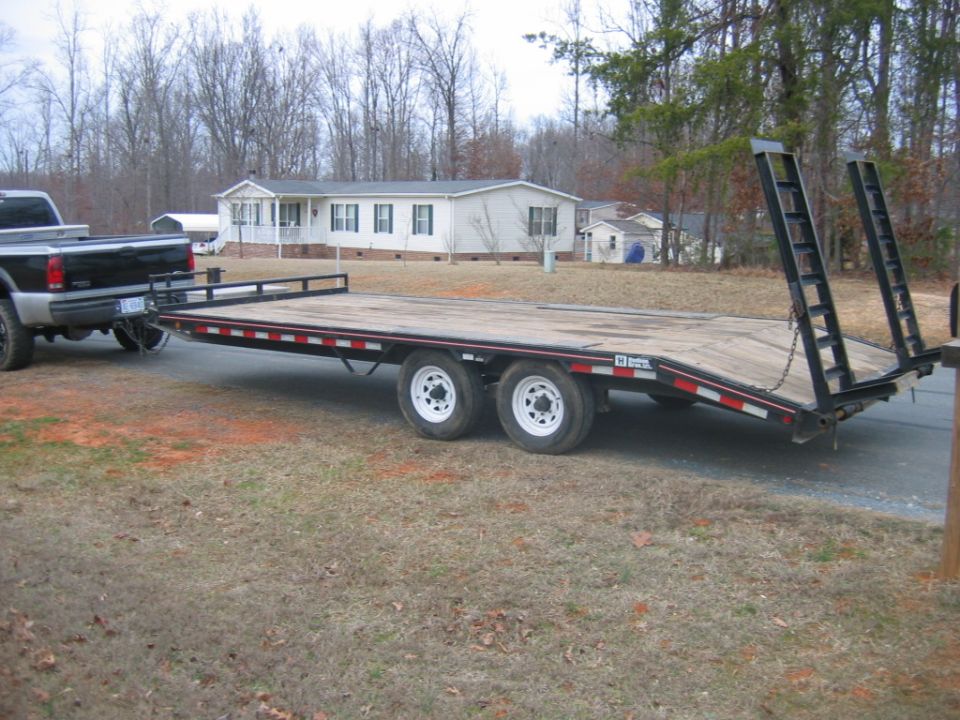 Pickup truck towing a flatbed trailer. Trailer has dual axles and ramps