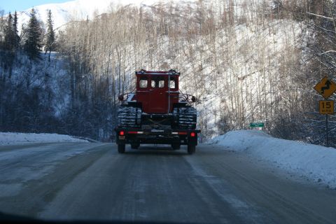 2003 Jeep TJ - A red tracked vehicle is transported on a trailer along a snow-covered highway.
