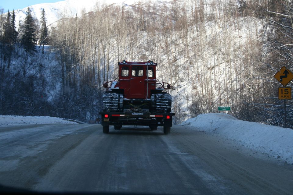 Red tracked vehicle with cab, loaded on a trailer, driving on a snowy road